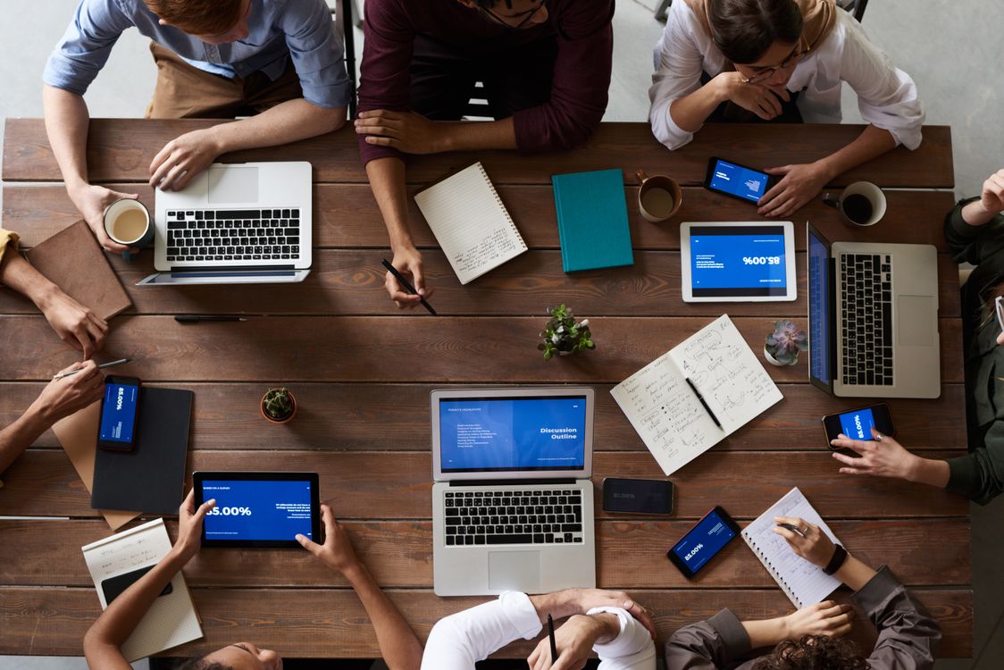 Overhead view of people planning together with laptops and notebooks around a table